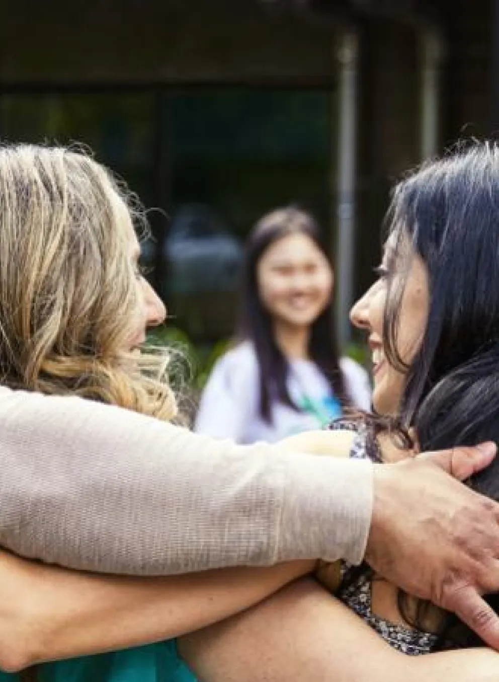 A group of diverse adults in a circle hug, displaying community and togetherness, with smiles indicating positive experience.